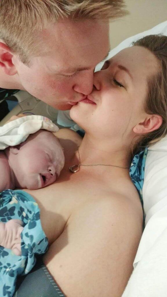 Husband kissing wife holding newborn baby