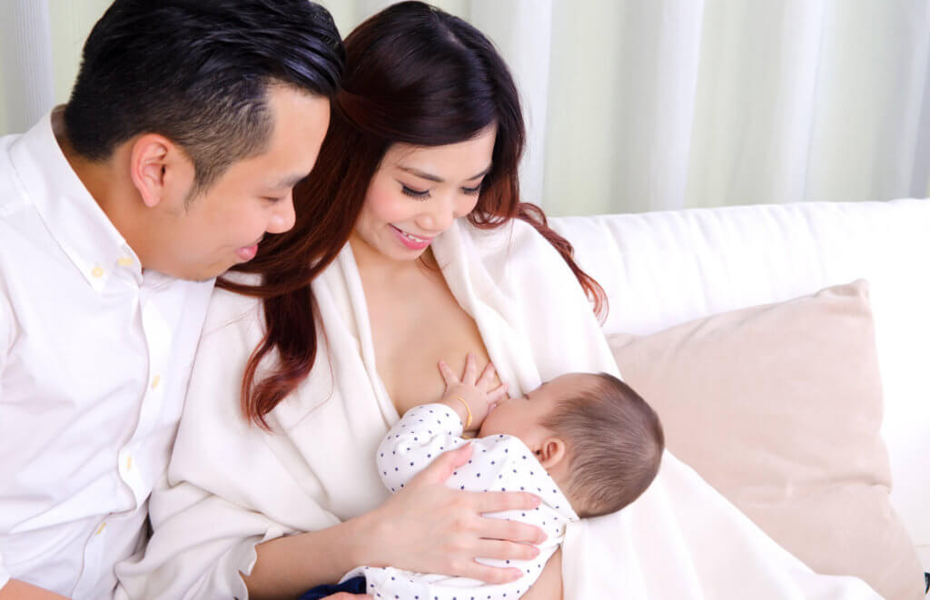 new parents holding baby while mother breastfeeds